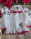 gemknits4kids baby girl wearing a white hand-knitted cardigan with floral embroidery, matching hat, and soft booties.