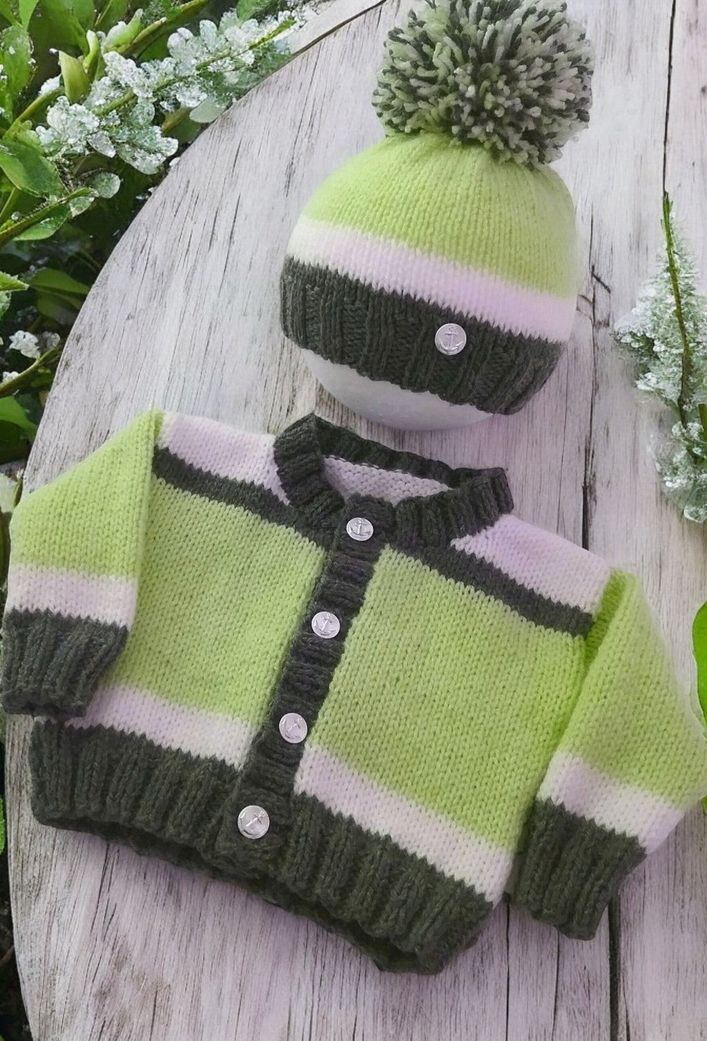 Baby boy wearing a gemknits4kids hand-knitted green, white, and grey block design cardigan and matching pom pom hat.