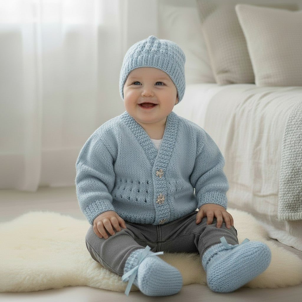 gemknits4kids baby boy wearing a light blue hand-knitted V-neck cardigan, matching beanie hat, and ribbon-tied booties.