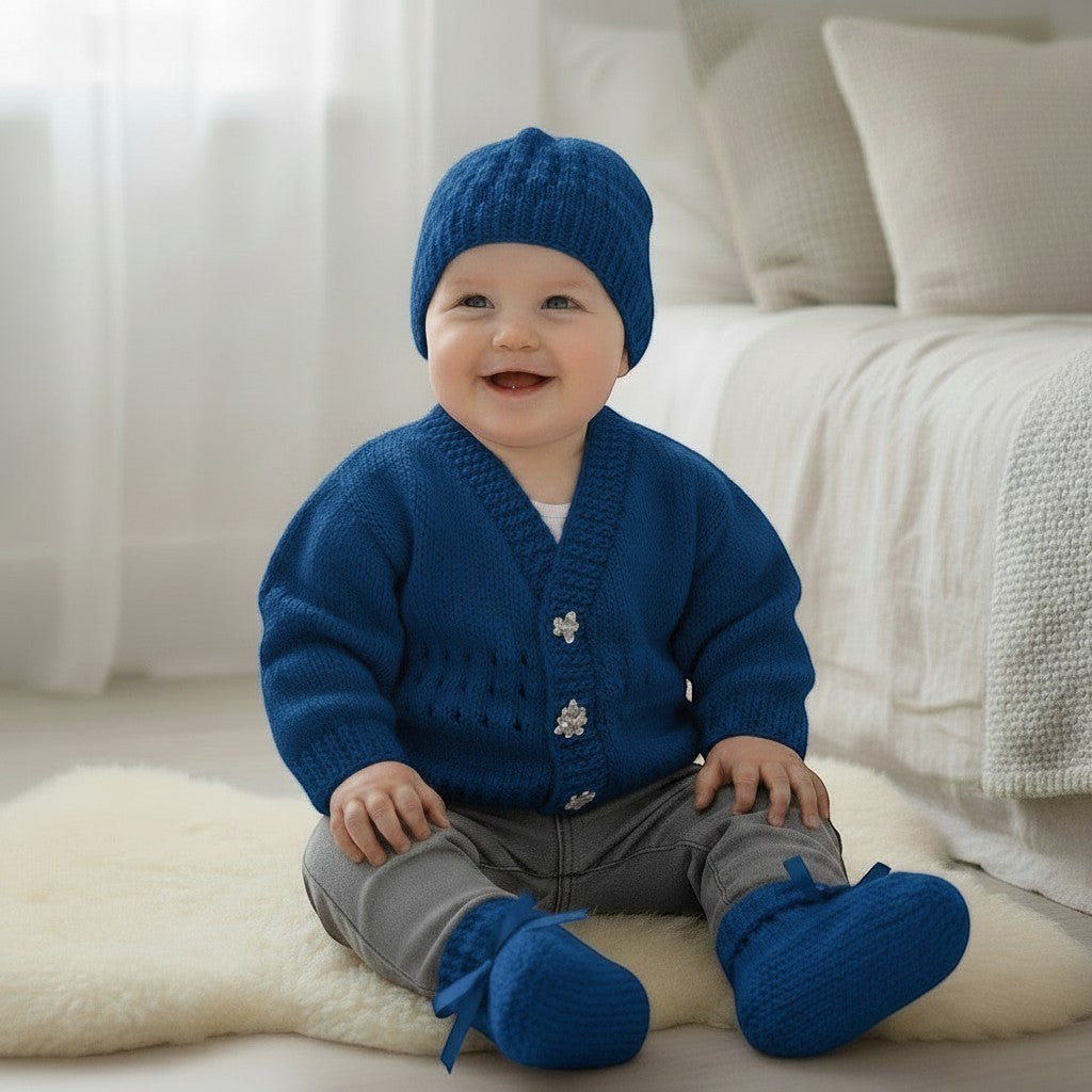 gemknits4kids baby boy wearing a blue hand-knitted V-neck cardigan, matching beanie hat, and ribbon-tied booties.