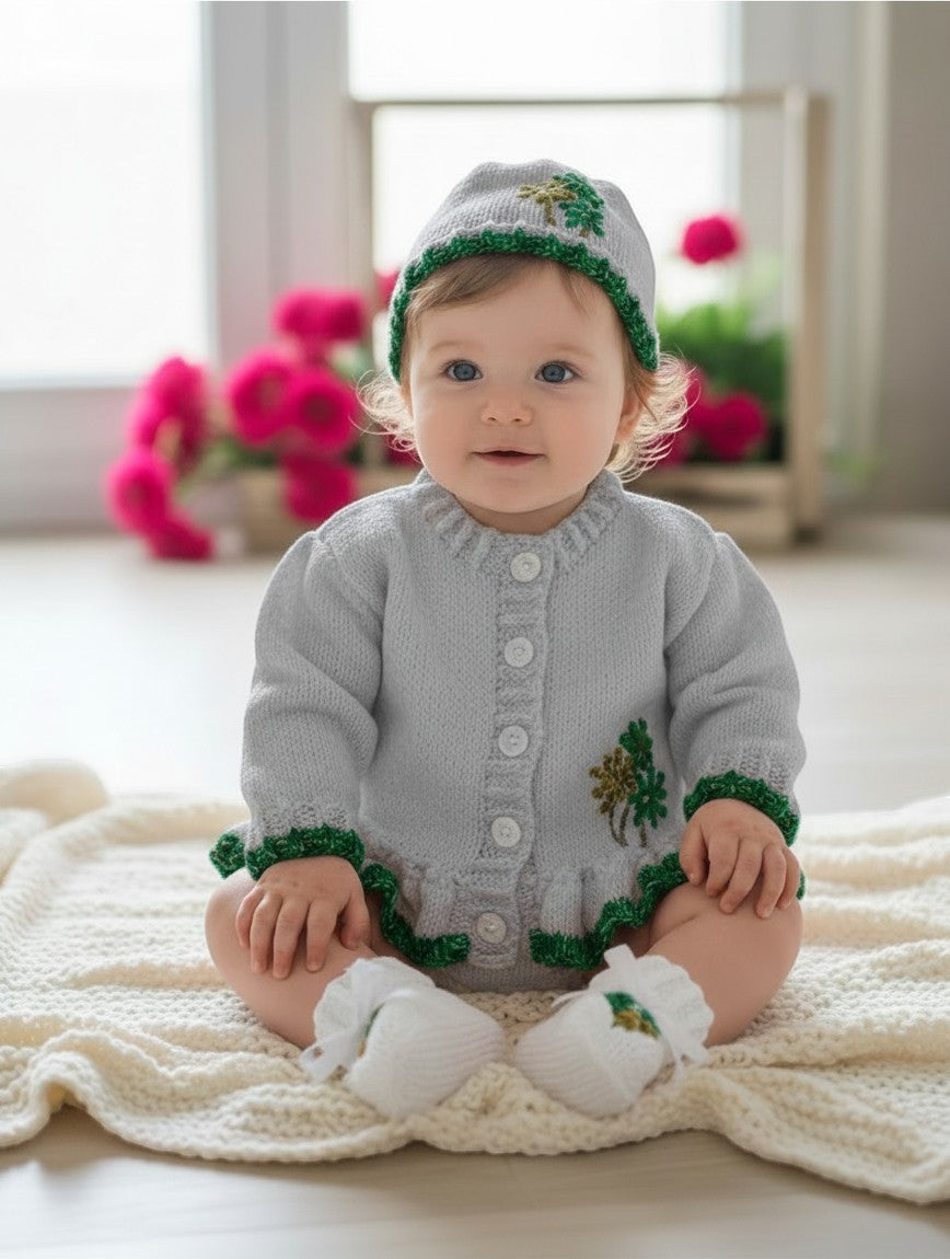 Baby girl wearing a gemknits4kids grey hand-knitted cardigan with green trim, matching hat, and white booties.