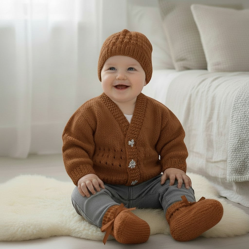 gemknits4kids baby boy wearing a hand-knitted brown V-neck cardigan, matching beanie, and ribbon-tied booties.