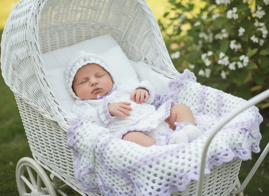 gemknits4kids baby girl in a white and lilac hand-knitted outfit with matching bonnet and pram cover in a carriage