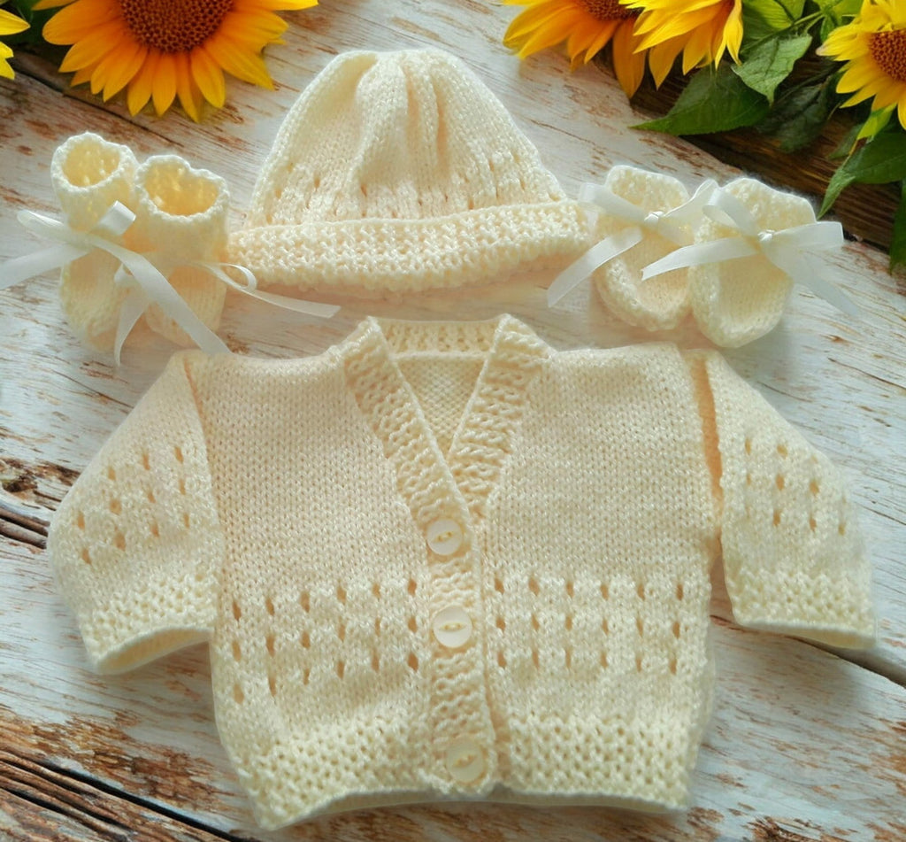gemknits4kids baby wearing a soft lemon hand-knitted cardigan, hat, and booties set sitting on a white rug in a bedroom.