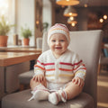 gemknits4kids baby wearing a cozy white knitted cardigan and matching hat with citrus-colored stripes on a chair