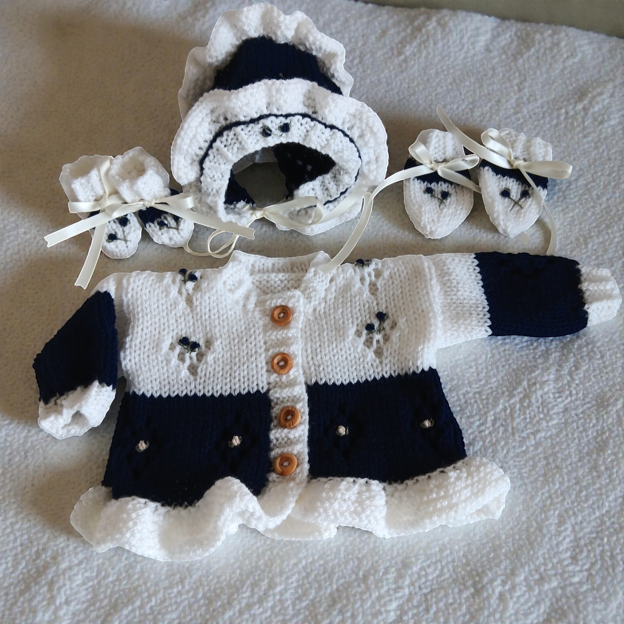 gemknits4kids two-tone navy and white hand-knitted baby cardigan set with frilly bonnet, mittens, and booties.
