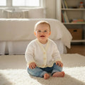 gemknits4kids hand knitted baby cardigan with scalloped hem worn by a smiling baby sitting on a rug
