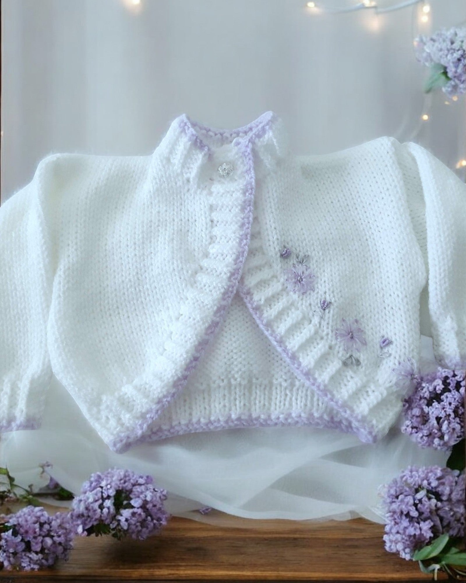 gemknits4kids white hand-knitted bolero cardigan with lilac embroidery worn by a toddler in a floral dress