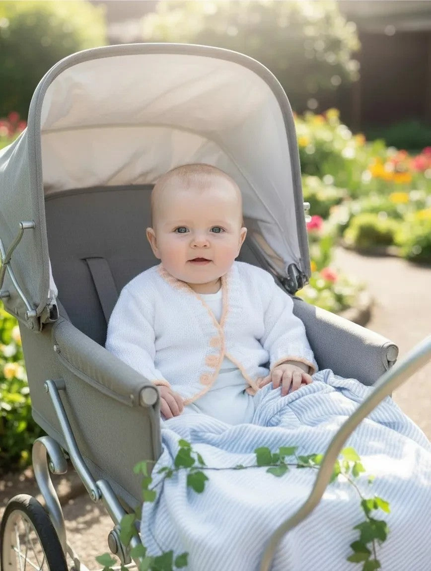 Baby sitting in a stroller wearing a white gemknits4kids hand knitted cardigan with a delicate scalloped hem