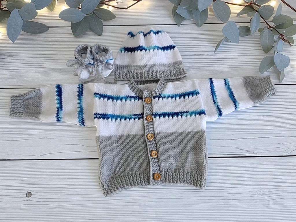 gemknits4kids baby boy wearing a hand-knitted grey & white striped cardigan, matching hat, and booties in a nursery